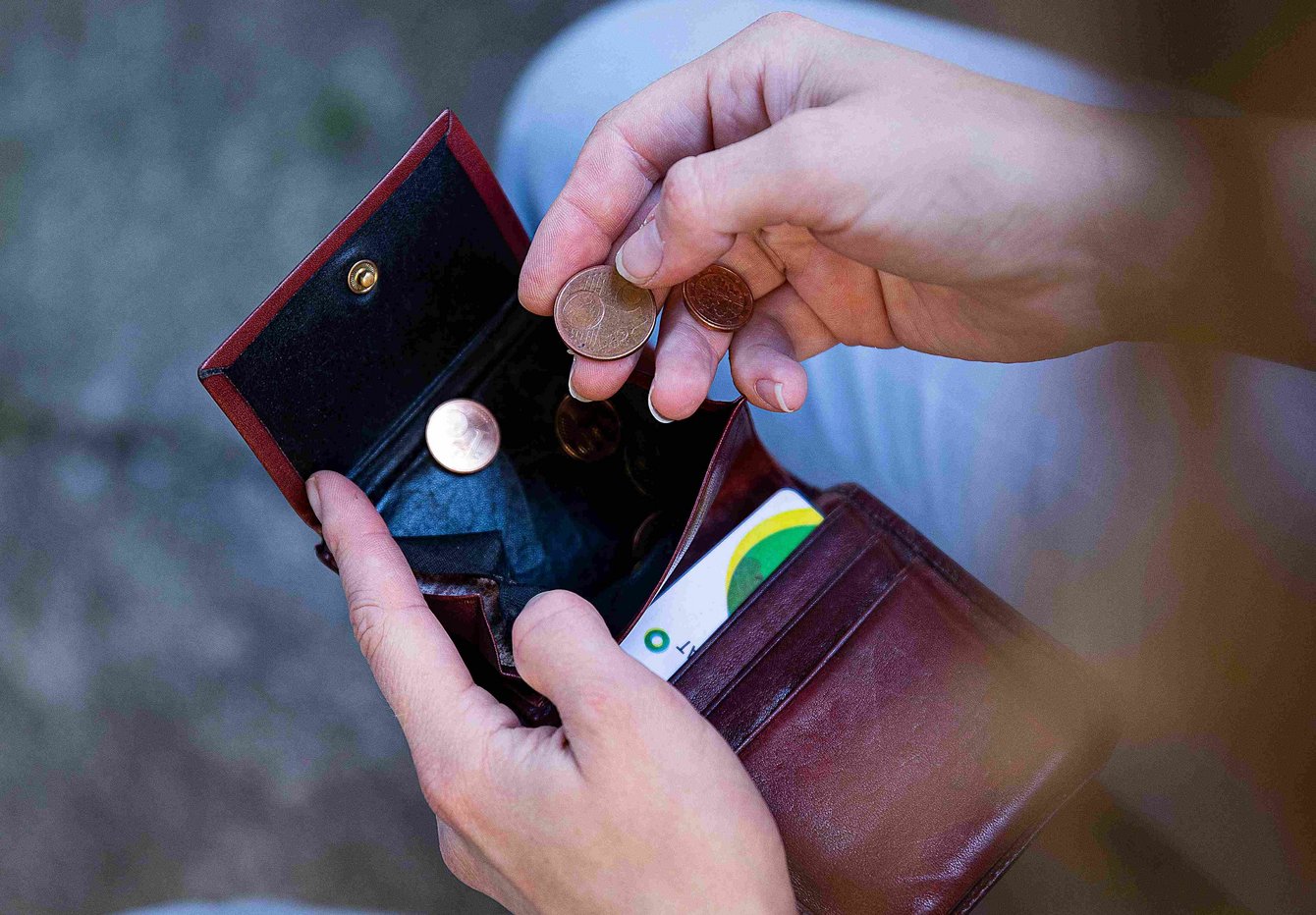 Eine Hand hält eine rote Geldbörse. Die andere Hand zählt die wenigen Münzen.