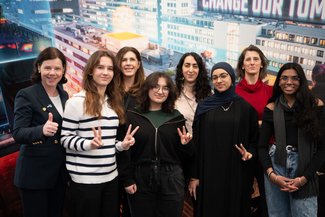 Barbara Czak-Pobeheim, Geschäftsführerin der FH Technikum Wien, posiert mit 6 Schülerinnen und Martina Fürpass vor einer Wand der FH Technikum mit dem Slogan "Change Our Tomorrow"