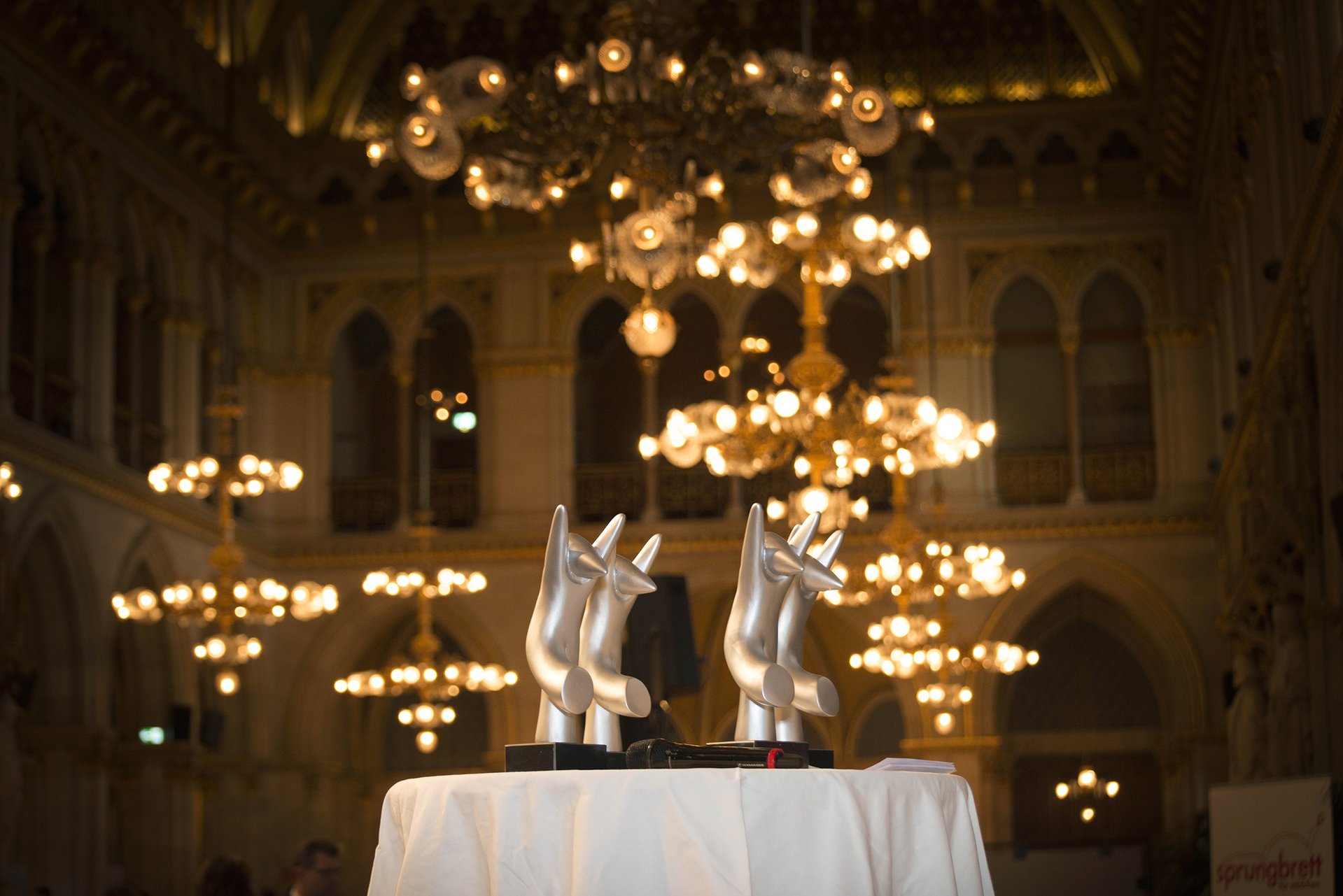 4 amaZone-Statuen auf einem Tisch in einem festlich beleuchteten Raum, im Hintergrund sind Kristallluster 
